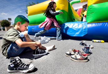 Elijah Martin, 7, ties his Chuck Taylor high-tops after having a go at the inflatable slide outside the Children's Library in Gallup on Saturday. The slide and other festivities were organized to kick off sign-ups for the children's summer reading program in Gallup. — © 2009 Gallup Independent / Adron Gardner 