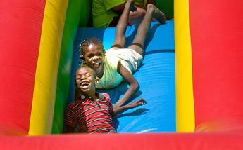 Evansky and Lily Kros enjoy a ride down the inflatable slide outside the Children's Library in Gallup on Saturday. The slide and other festivities were organized to kick off sign-ups for the children's summer reading program in Gallup. — © 2009 Gallup Independent / Adron Gardner 