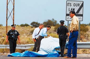 Richard Malone of the Office of Medical Investigator and Assistant District Attorney Alex Beattie look under a tarp where the body of Vivian Williams lay at exit 63 on Interstate 40 in Prewiit. — © 2009 Gallup Independent / Brian Leddy 