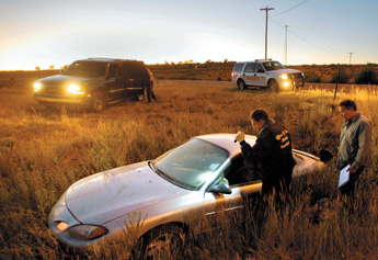 Office of the Medical Investigator Richard Malone, left, and Assistant DA Alex Beattie examine the car of a suspect in a double hit and run fatality on N.M. 264 in Yatahey.— © 2009 Gallup Independent / Adron Gardner 