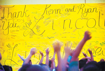 Students raise their hands in front of a banner thanking Kevin and Ryan Menapace during an assembly held to honor the Menapaces at Lincoln Elementary Friday. The two men rescued two Lincoln students and their sibling from their burning home Aug. 7. — © 2009 Gallup Independent / Cable Hoover 