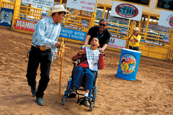 Kriston Tyler gets a ride from teacher Fred Charley while Roman McCabe runs next to him during the Exceptional Children's Rodeo on Friday. — © 2009 Gallup Independent / Brian Leddy 