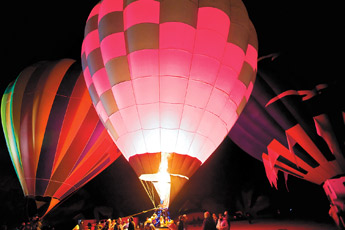 A crowd of spectators and crew are illuminate by the balloons during the Red Rock Balloon Rally Glow in the Rocks at Red Rock Park Friday night. — © 2009 Gallup Independent / Cable Hoover 